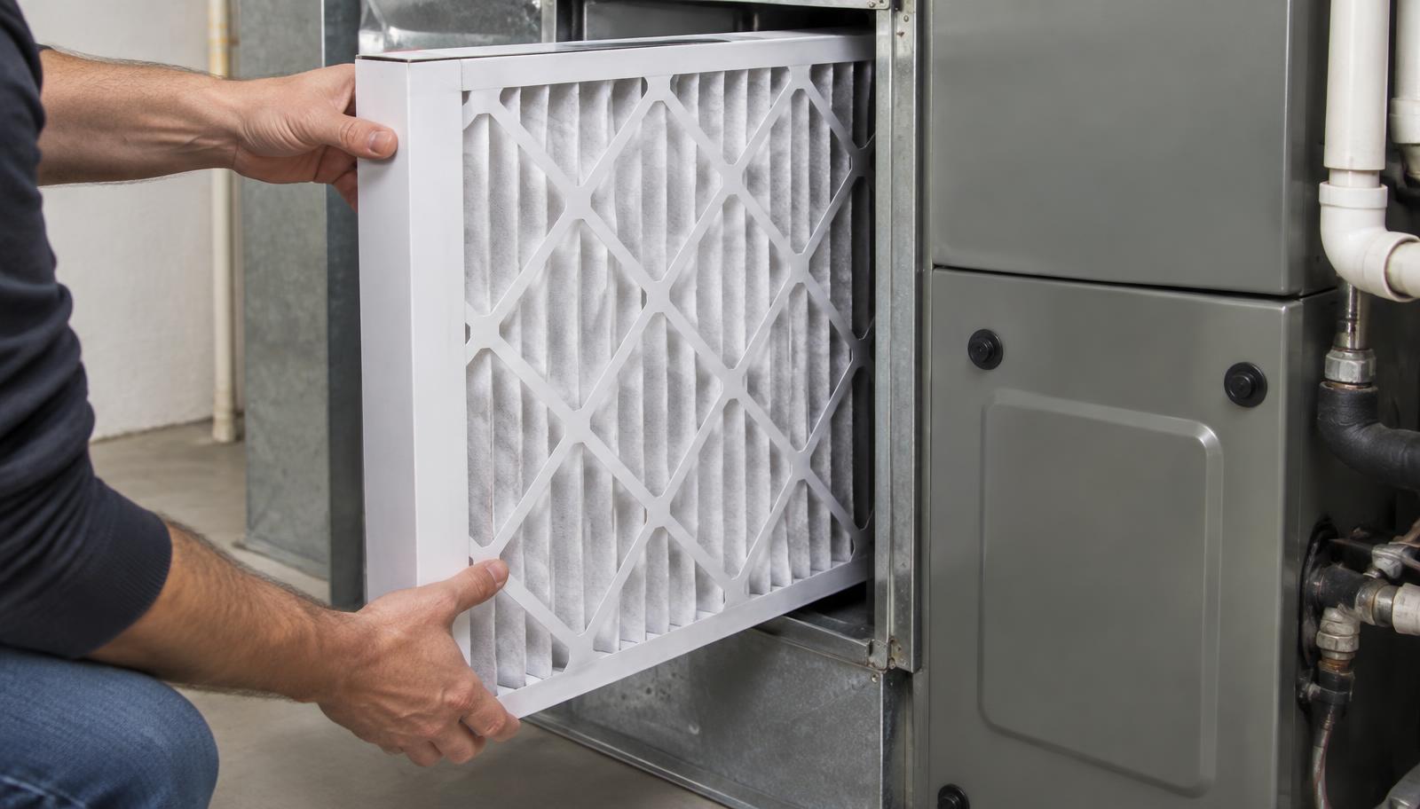 Technician installing a MERV 13 whole-home media filter in a furnace filter cabinet